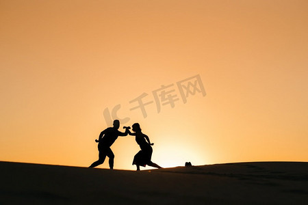 沙漠中一对幸福的年轻夫妇在橙色落日的背景下的剪影