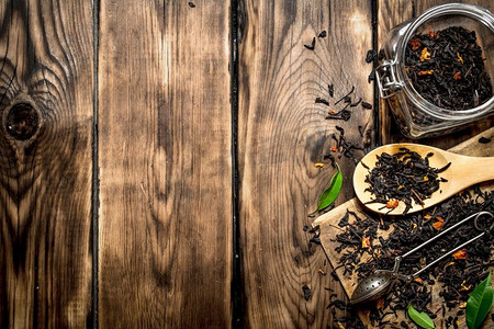 木质茶匙摄影照片_有茶匙和绿叶的干茶壶。在木质背景上..干茶缸