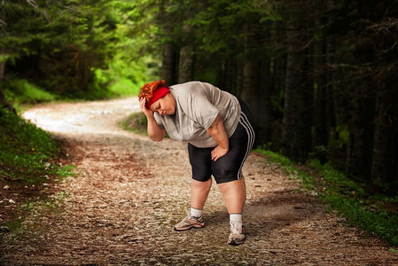跑步卡路里摄影照片_超重的女人在森林里跑步后疲惫不堪。燃烧卡路里。女性肥胖，暴食症。吃不健康的食物