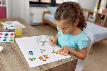 童年，爱好和休闲概念—小女孩用画笔画木纸板项目在家里。小女孩在家里画木制物品