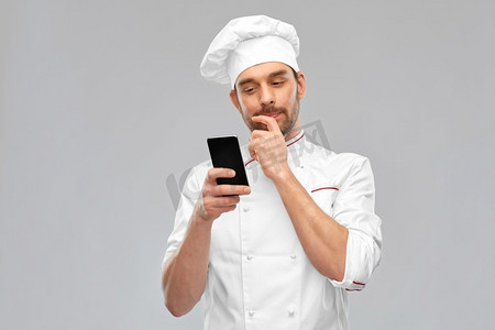 烹饪，烹饪和人的概念—男厨师戴帽有智能手机在灰色背景男厨师与智能手机