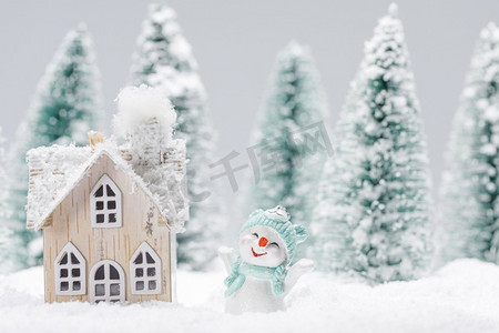 冬季背景与雪人摄影照片_小装饰雪人与礼物在冷杉林附近的木屋在落雪。冬天的雪人和房子