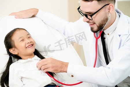 年轻的男医生在医院的办公室里给小孩子做检查。这孩子很开心，也不怕医生。医疗儿童保健理念。