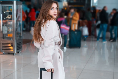 在现代机场，身穿白大褂的年轻女子，人们带着行李出行。在后台排队登记。