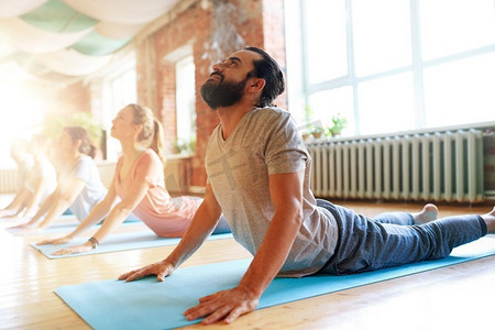 健身，瑜伽和健康的生活方式概念—一组人做眼镜蛇姿势在垫子在工作室。一组人做瑜伽眼镜蛇姿势在工作室