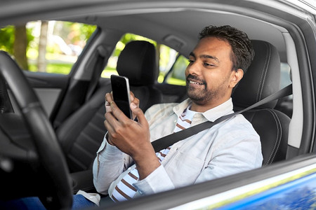 交通、人和科技概念-微笑的印度男人或司机在车内使用智能手机。微笑的印度男子在车里使用智能手机