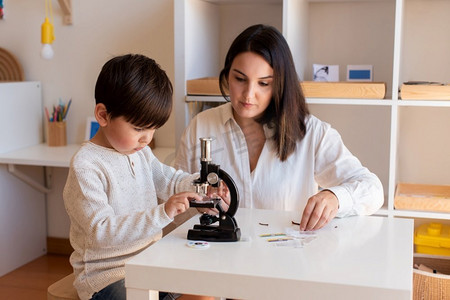 Lillte孩子在显微镜下探索科学，母亲或老师的帮助。家务活。学习社区。蒙特梭利学校