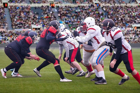 一群年轻的职业美式橄榄球运动员在体育场上比赛，观众站在背景中