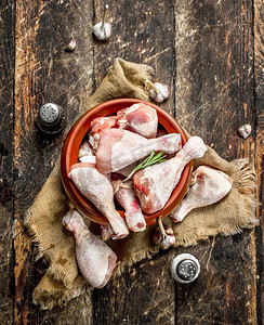 温暖的大鸡腿摄影照片_生鸡腿与大蒜和香料在碗中。在木制背景上。生鸡腿与大蒜和香料在碗中。