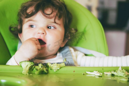 婴儿吃食物在她的绿色高脚椅