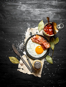 早上吃早餐。炒鸡蛋和培根豆。在一个黑色的木背景。早上吃早餐。炒鸡蛋和培根豆。