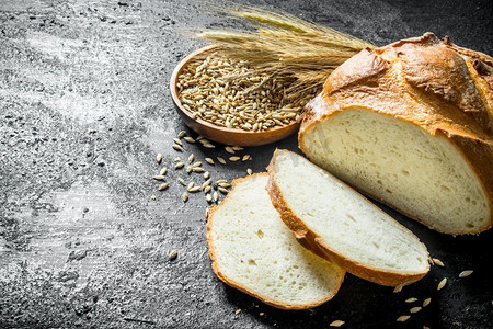 卡通面包切片装饰摄影照片_新鲜面包片与小穗和谷物。在黑色的乡村背景。新鲜面包片与小穗和谷物。