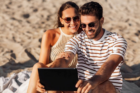 休闲与人的概念-在夏日海滩与平板电脑幸福的情侣。夏日海滩上，一对幸福的夫妇带着平板电脑