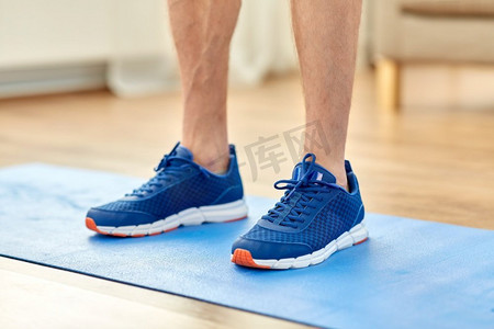 运动鞋摄影照片_健身，运动和鞋概念—关闭男性脚在蓝色运动鞋在练习垫。关闭男性脚在运动鞋上的运动垫