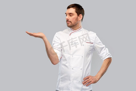 烹饪，烹饪和人的概念—男子厨师在夹克拿着东西在灰色背景的手。男厨师手里拿着东西