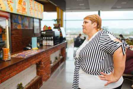 快餐店菜单上的胖女人。超重女性购买快餐，肥胖问题。快餐店菜单上的胖女人
