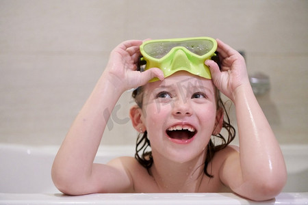 暑假游泳摄影照片_有通气管护目镜的小女孩在浴缸里洗澡时在浴缸里，孩子们卫生概念和暑假在电晕病毒留在家里