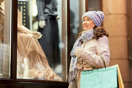 节日和人们的概念快乐女人拿着购物袋在冬城的橱窗里看着。冬天提着购物袋的快乐女人