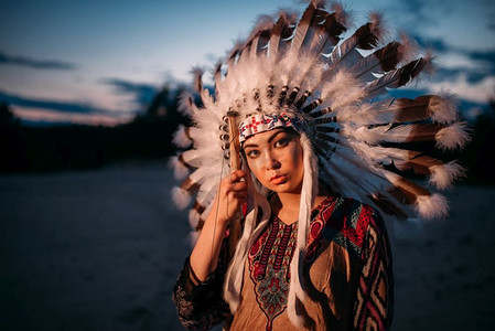 羽毛扇简笔画摄影照片_肖像的年轻的美国印第安妇女日落。切罗基族，纳瓦霍族，西部土著文化。用野鸟羽毛制成的头饰。 