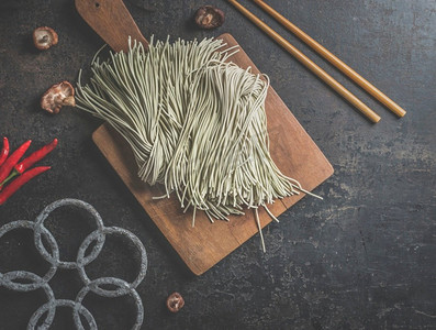 筷子上的面摄影照片_生自制亚洲面条在黑暗的厨房桌子上用筷子。俯视图