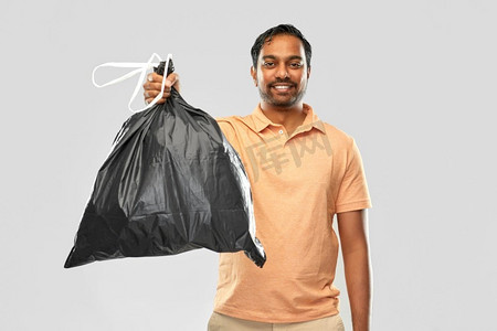 回收，分类和可持续性概念—微笑的年轻印度人持有垃圾袋在灰色背景。微笑的印度男子拿着垃圾袋