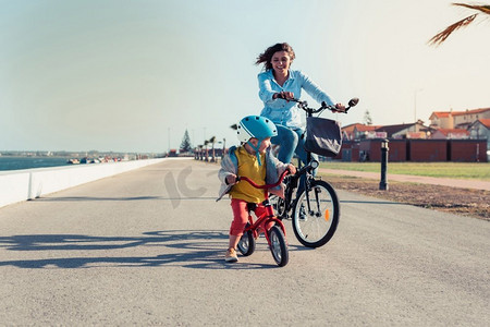 小孩子骑平衡自行车与他的母亲在一个城市公园的自行车