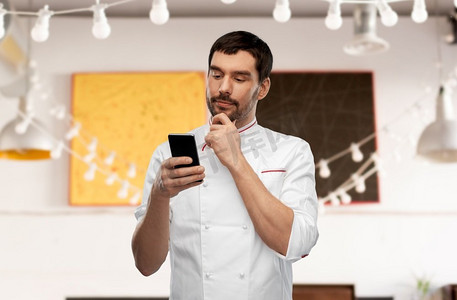 烹饪，烹饪和人的概念思考男性厨师与智能手机在餐馆背景。思考男性厨师与智能手机