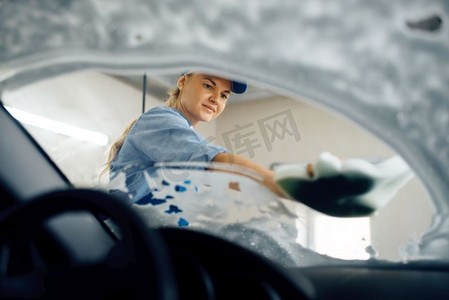 女洗衣机用海绵擦拭汽车挡风玻璃，从内部视图，洗车。妇女清洁车辆，洗车站，洗车业务