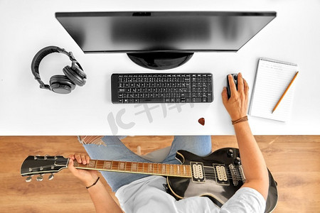 音乐在线摄影照片_休闲，音乐和人的概念—年轻人或音乐家与电脑和吉他坐在桌子。年轻人与电脑和吉他在桌子上
