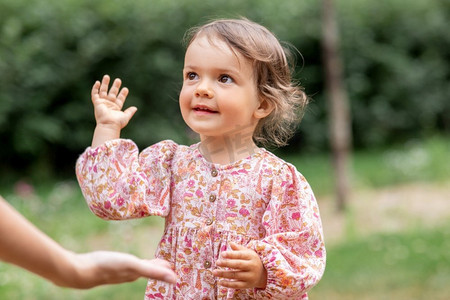 伸出手摄影照片_童年、休闲和人的概念--快乐微笑的小女婴牵起手来。快乐微笑的小女孩向成人伸出手