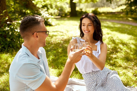 休闲和人的概念快乐的夫妇与饮料在夏季公园野餐。一对幸福的情侣在夏季公园敬酒