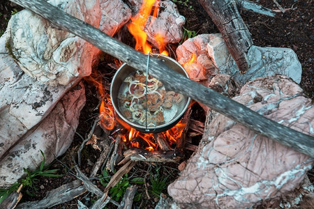 在徒步旅行中露营燃烧的篝火的火的旅游水壶。在森林里用木柴做饭。