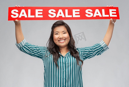 购物和人概念—愉快的微笑的年轻亚洲妇女有销售横幅在灰色背景快乐的微笑的年轻亚洲妇女与销售横幅