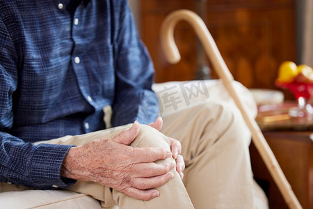 在家里坐在沙发上因关节炎导致膝痛的老人的特写镜头美女牛仔裤