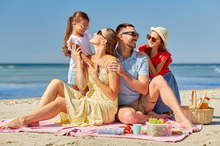 家庭、休闲和人的概念-快乐的母亲、父亲和两个女儿在夏季海滩野餐。快乐的一家人在夏日海滩野餐