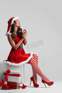 美丽的圣诞小女孩在红色圣诞老人礼服和条纹长袜与礼品盒。圣诞女孩与礼物