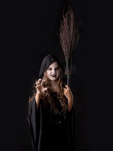 女孩在万圣节邪恶愤怒的女巫服装微笑咆哮举行扫帚在黑色背景隔绝。女孩在万圣节女巫服装