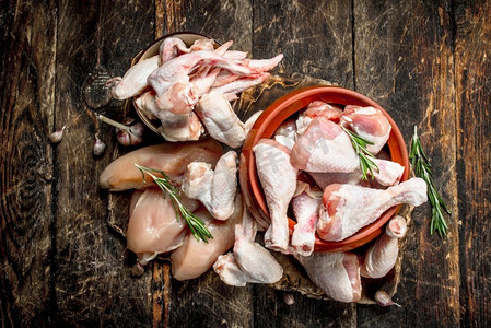 鸡腿背景摄影照片_各种类型的生鸡肉和草药放在碗里。在木质背景上..各种类型的生鸡肉和草药放在碗里。