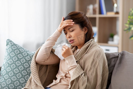 健康、寒冷和人的概念-悲伤的生病的年轻亚洲妇女在家里用纸巾头疼。生病的亚裔妇女在家中头痛