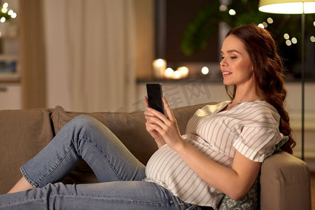 怀孕，技术和人的概念—快乐的孕妇与智能手机在家里。快乐的孕妇与智能手机在家里
