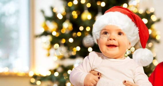 假日和童年概念—微笑的女婴在圣诞树灯圣诞帽。微笑的女婴在圣诞树灯