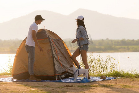 年轻的成年亚洲夫妇投球和建立帐篷露营湖。露营之旅与狗户外活动露营地概念。