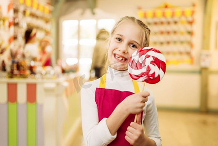 手拿棒棒糖摄影照片_快乐的小女孩在棍子上拿着手工糖焦糖.美女儿童