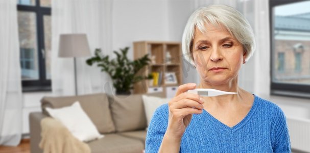 健康、老年和人的概念-患病的老年妇女，在家庭起居室背景上有体温计。带着体温计的患病老年女性