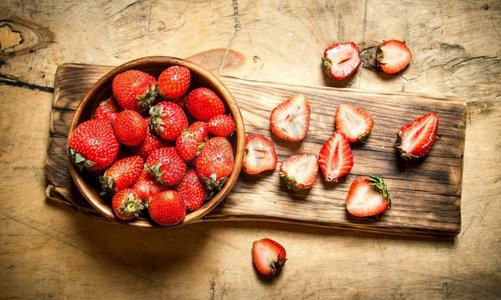木质背景摄影照片_成熟的草莓放在船上的碗里。在木质背景上..成熟的草莓放在船上的碗里。