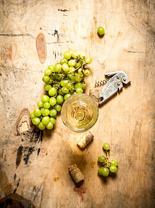 绿色加黄色摄影照片_一杯加葡萄和开瓶器的白葡萄酒。在木质背景上..一杯加葡萄和开瓶器的白葡萄酒。