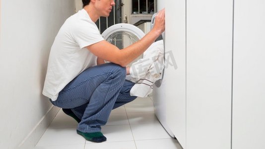 加衣服摄影照片_男人把衣服放洗衣机。高分辨率照片。男人把衣服放洗衣机。高品质的照片