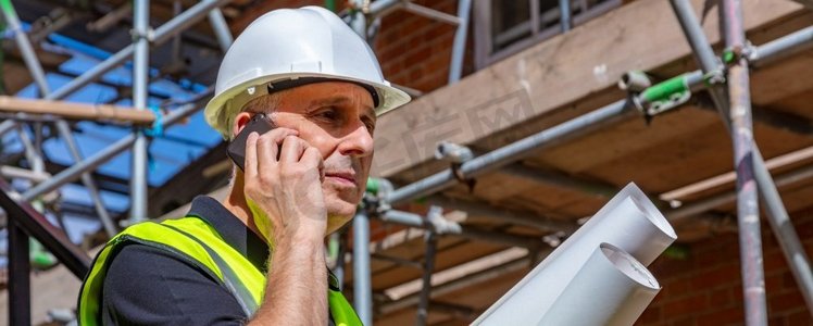 男性建设者工头，工人或建筑师在建筑工地举行建筑计划和谈话在他的手机全景网横幅标题