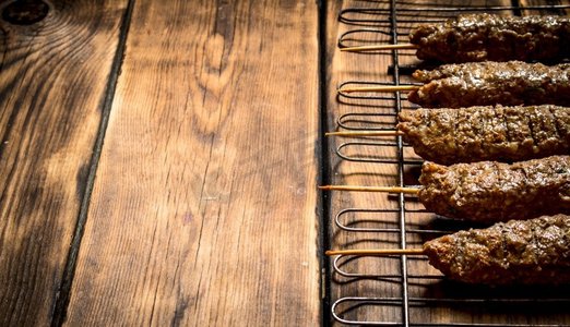 土耳其烤肉摄影照片_烤肉串在烤架上。在一张木桌上。烤肉串在烤架上。