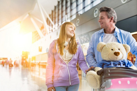 成熟男子推行李车的肖像，而走在与她的女儿在机场与镜头耀斑